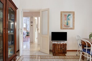 A room with a television on a wooden stand, a dining table with chairs, and a cabinet with glass doors. - Seba House Apartment with Private Terrace, Wi-Fi and Air Conditioning (La spezia)