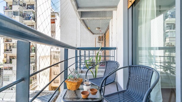 A balcony with a table, two chairs, a potted plant, and a view of a cityscape. - Charming studio on Las Heras Avenue, Recoleta | 4P (Ciudad Autónoma de Buenos Aires)