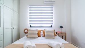 A neatly made bed with white and striped pillows, a bedside table with a lamp, and a window with blinds. - Charming 2-Bedroom Apartment | Renovated | Cañitas (Ciudad Autónoma de Buenos Aires)