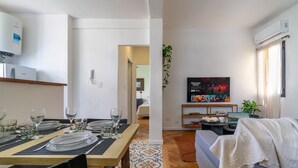 A dining area with a wooden table set for four, a kitchen with an air conditioner, and a living area with a sofa and a TV. - Charming 2-Bedroom Apartment | Renovated | Cañitas (Ciudad Autónoma de Buenos Aires)