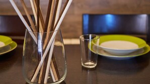 A dining table with a clear glass vase containing wooden sticks, a glass, and green plates. - AV Soterra a 2B in Vila (Ávila)
