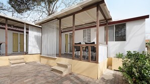 Un espacio al aire libre cubierto con escalones que llevan a una puerta, una zona de estar con sillas y una ventana.
