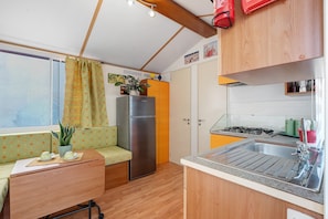Eine kleine Küche mit Kühlschrank, Spüle und einem Fenster mit Vorhängen.