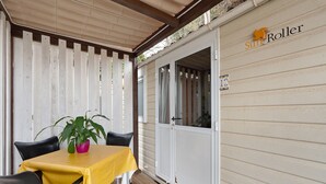 En overdækket terrasse med et bord, stole, en potteplante og en skydedør med et nummer.