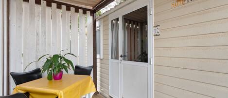 A covered patio with a table and chairs, a potted plant, and a sliding door with a number.