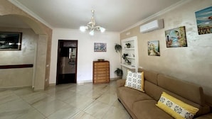 A spacious living room with a beige sofa, a wooden cabinet, and a chandelier. - From Pupa SeaView Apartment (Vico Equense)