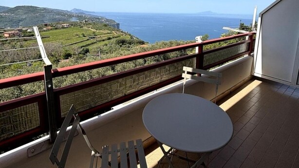A balcony with a white table and chair, overlooking a coastal landscape with hills and the sea. - From Pupa SeaView Apartment (Vico Equense)