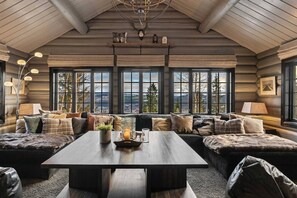 A log cabin interior with a large window, a wooden table, and a sofa.