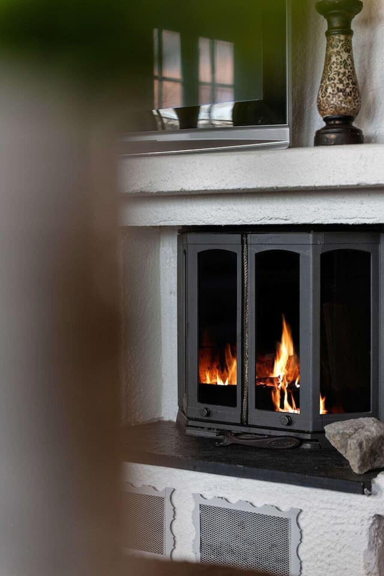 A fireplace with a visible fire, a stone mantelpiece, and a decorative vase.