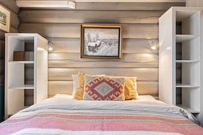 A bedroom with a bed, a framed picture on the wall, and built-in shelving on either side.