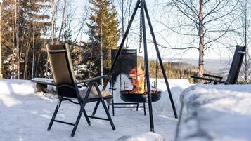A snow-covered outdoor area with a fire pit and two chairs.