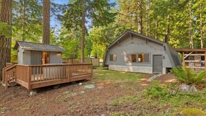 A cabin with a wooden deck and a separate shed, surrounded by a forest. - Serene 1-bedroom cabin in charming Ashford perfect for getaway (Ashford)