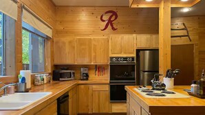 A compact kitchen with wooden cabinets, a stainless steel refrigerator, a microwave, and a stove. - Serene 1-bedroom cabin in charming Ashford perfect for getaway (Ashford)