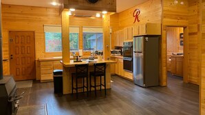 A wooden cabin-style kitchen with a central island, a refrigerator, and a microwave. - Serene 1-bedroom cabin in charming Ashford perfect for getaway (Ashford)