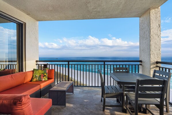 Uma varanda com vista para o oceano, um sofá, uma mesa e cadeiras.