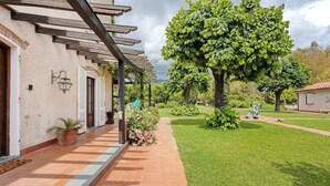 A covered outdoor area with a brick pathway, potted plants, and a large tree. - Room 'Camera Alex - Marinsky' with Shared Garden, Wi-Fi and Air Conditioning (Pietrasanta)