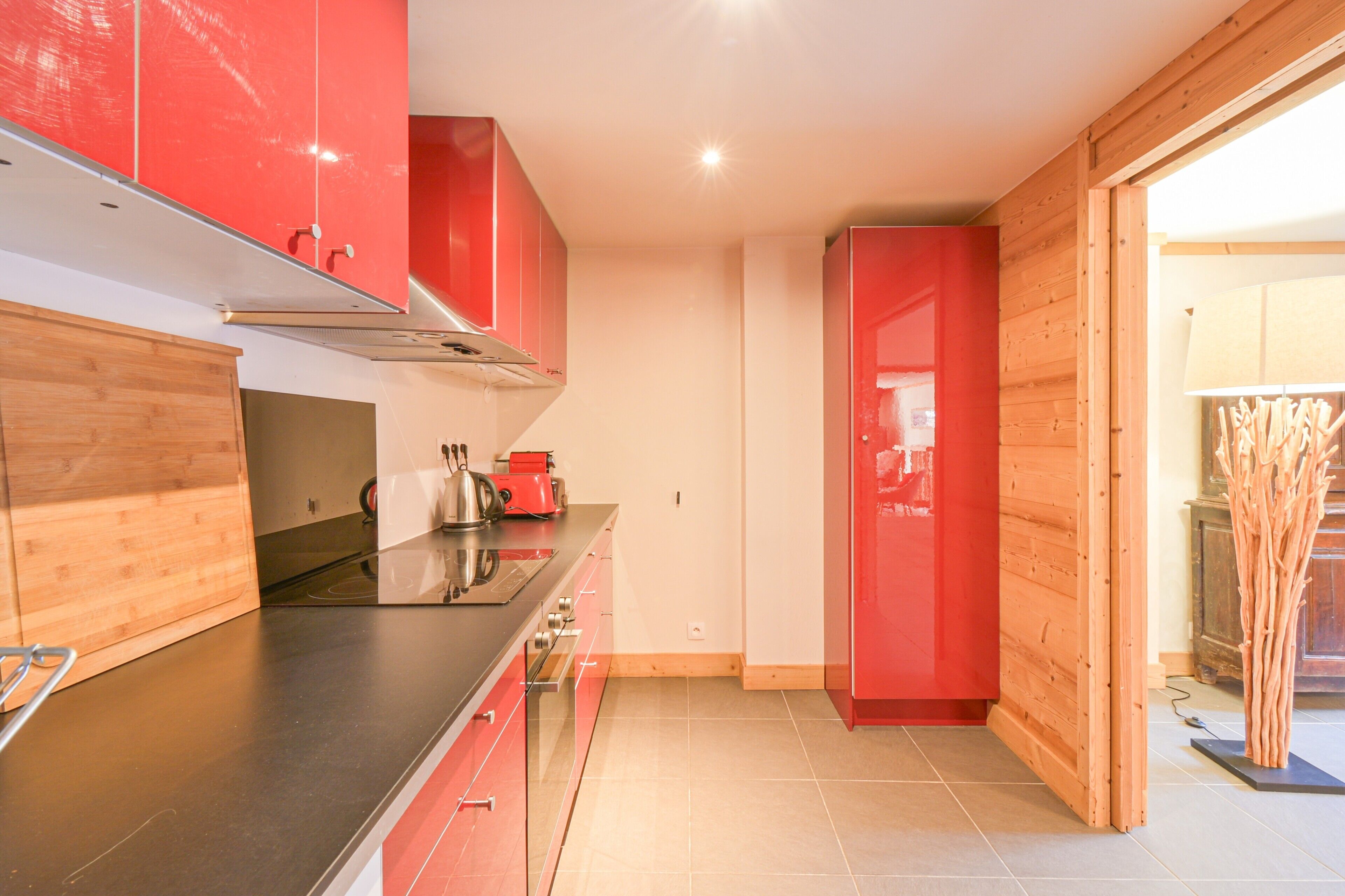 A modern kitchen with red cabinets, a black countertop, and a wooden floor.