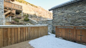 Una terraza de madera que conduce a un edificio de piedra, con una valla de madera y una escalera.