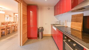 Cocina compacta con armarios rojos, una campana extractora de acero inoxidable y una tabla de cortar de madera.
