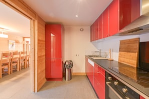 Une cuisine de taille réduite avec des meubles de couleur rouge, une hotte de cuisine en acier inoxydable et une planche à découper en bois.