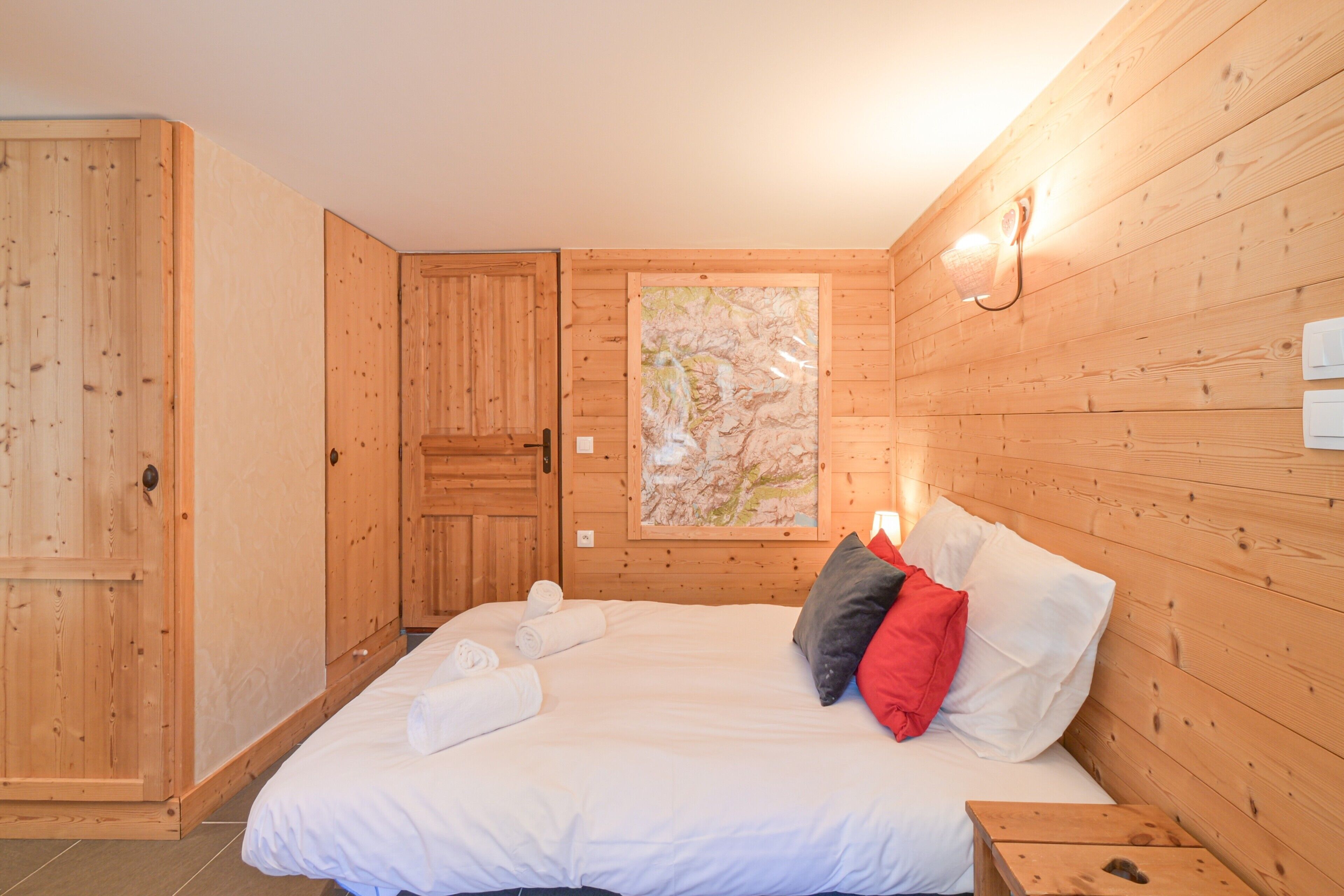 Une pièce aux murs lambrés, avec un lit, une carte accrochée au mur et une porte.