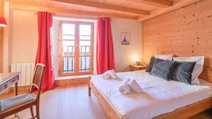 Una habitación con paneles de madera, una cama, una silla, un escritorio y un ventanal con cortinas.