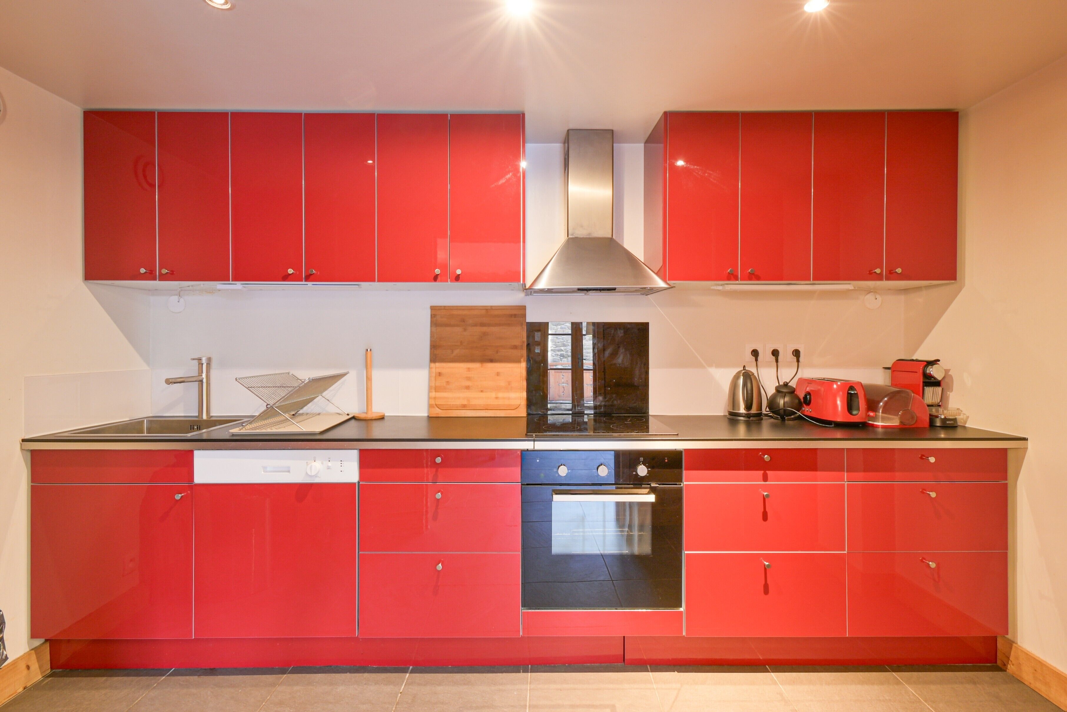 A kitchen with red cabinets, a dishwasher, an oven, and a stainless steel range hood.