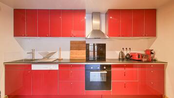 A kitchen with red cabinets, a dishwasher, an oven, and a stainless steel range hood.