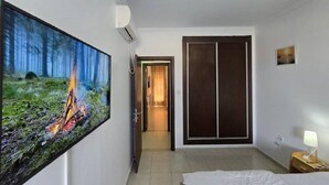 A hotel room with a bed, a painting of a forest fire, a wardrobe, and a door leading to another room.