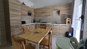 A modern kitchen with wooden cabinetry, a dining table with chairs, and a baby high chair.