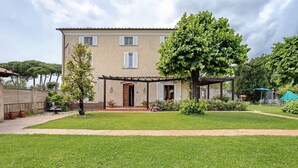 Ein zweistöckiges Haus mit Veranda, einem Baum im Garten und einer Pergola.