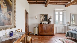 Ein Zimmer mit einem Holztisch, Stühlen, einem Schrank, einem Gemälde und einem Bett mit einem gemusterten Überwurf.