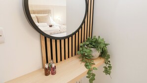 A bedroom with a round mirror, a bed with white bedding, a bedside lamp, and a wooden shelf with toiletries and a potted plant. - Loco Lodge (Keighley)