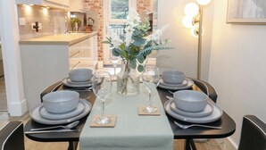A dining area with a brick wall, a view of the kitchen, and a table set with plates, glasses, and a vase of flowers. - Loco Lodge (Keighley)