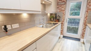 A modern kitchen with a wooden countertop, stainless steel sink, and a brick accent wall. - Loco Lodge (Keighley)