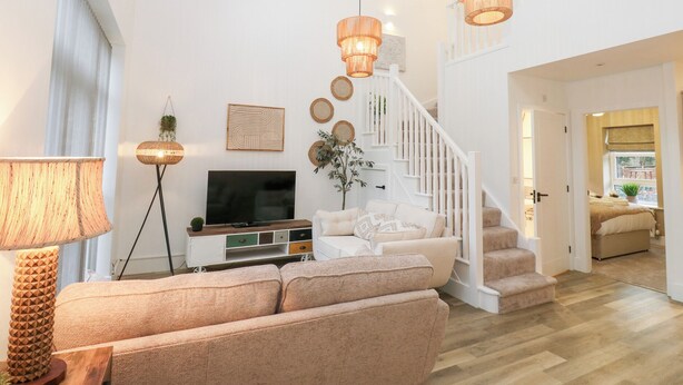 A modern living room with a sofa, TV, and decorative items. A staircase leads to another room. - Loco Lodge (Keighley)