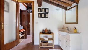 Un couloir menant à une salle de bain équipée d’une étagère en bois, d’un miroir et de tableaux encadrés accrochés au mur.