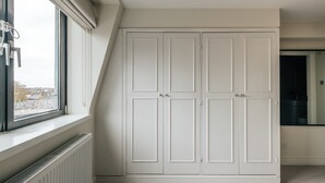 Ein Zimmer mit einem großen weißen Kleiderschrank, einem Heizkörper und einem Fenster mit Blick auf Gebäude.