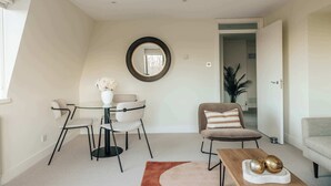 Ein modernes Wohnzimmer mit einem runden Spiegel, einem Esstisch mit Stühlen, einer Couch und einem Couchtisch mit Dekoration.
