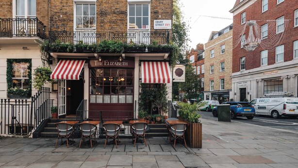 Ein Backsteinhaus mit einem Café namens 'The Elizabeth' im Erdgeschoss, das Außenplätze und eine rot-weiß gestreifte Markise bietet.