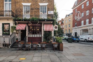 A brick building with a ground-floor cafe named 'The Elizabeth' featuring outdoor seating and a red and white striped awning. - The Eccleston  - Belgravia 1BD Apartment (London)