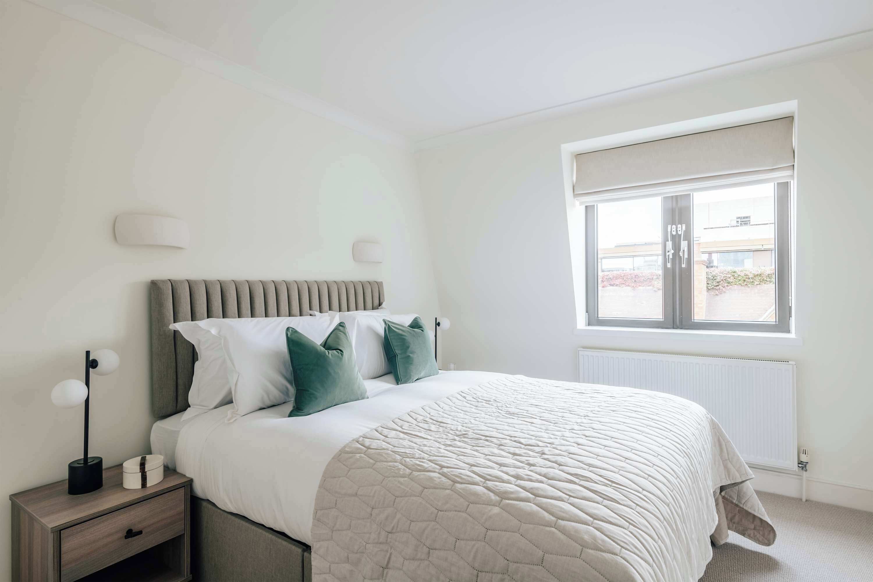Ein Schlafzimmer mit Bett, Nachttisch, Lampe und Fenster.