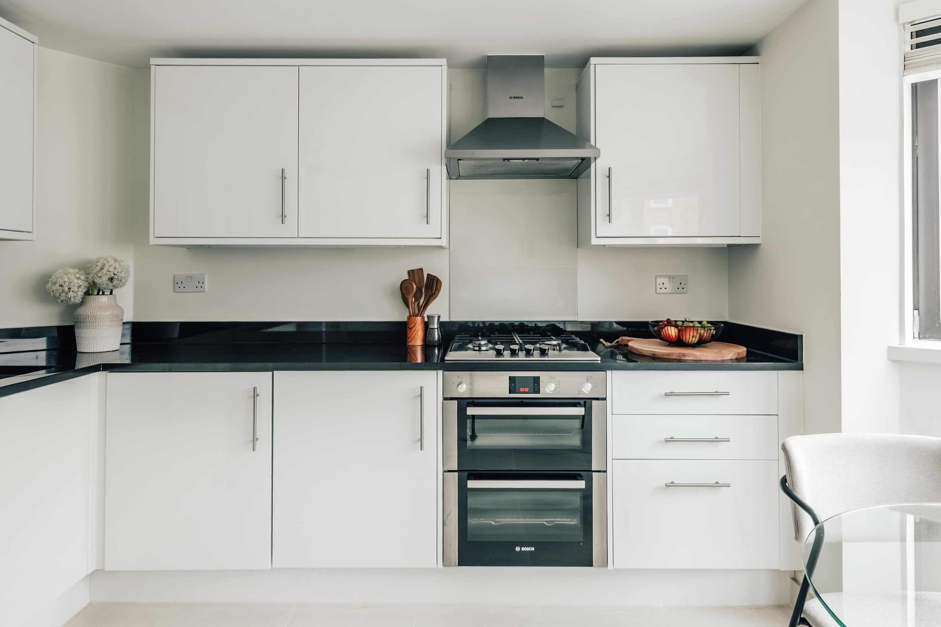 Een moderne keuken met witte kastjes, een zwart aanrecht, een gasfornuis van Bosch en twee ovens.