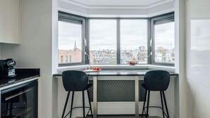A modern kitchen with a bay window, two black chairs, a countertop, and a coffee machine. - The Eccleston: Elegant 2BR Flat in Prime Belgravia (London)