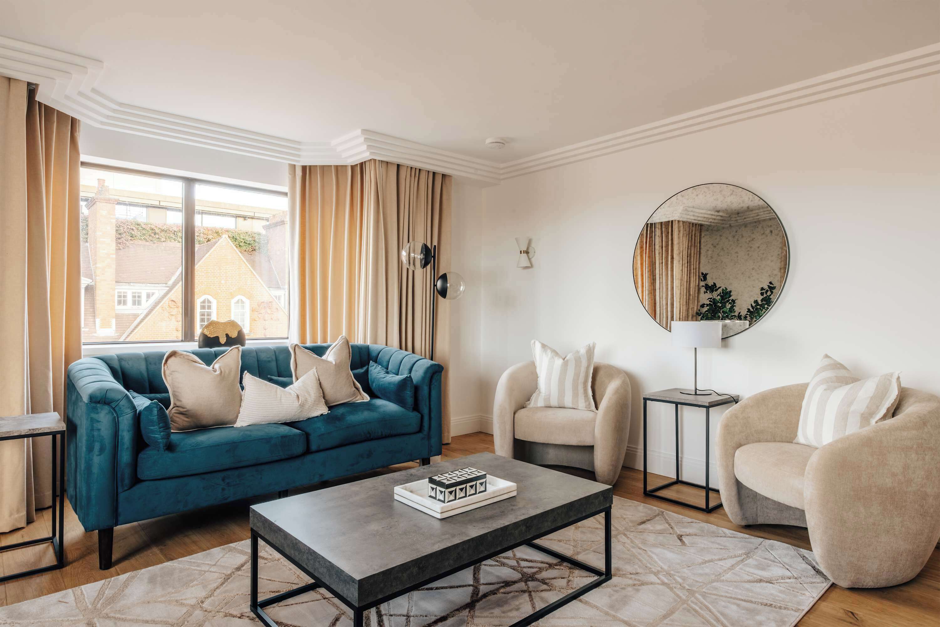 Una sala de estar con un sofá azul, sillones color beige, una mesa de centro y un espejo redondo en la pared.