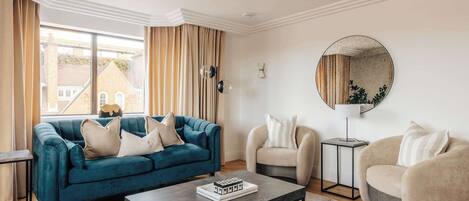 Una sala de estar con un sofá azul, sillones color beige, una mesa de centro y un espejo redondo en la pared.
