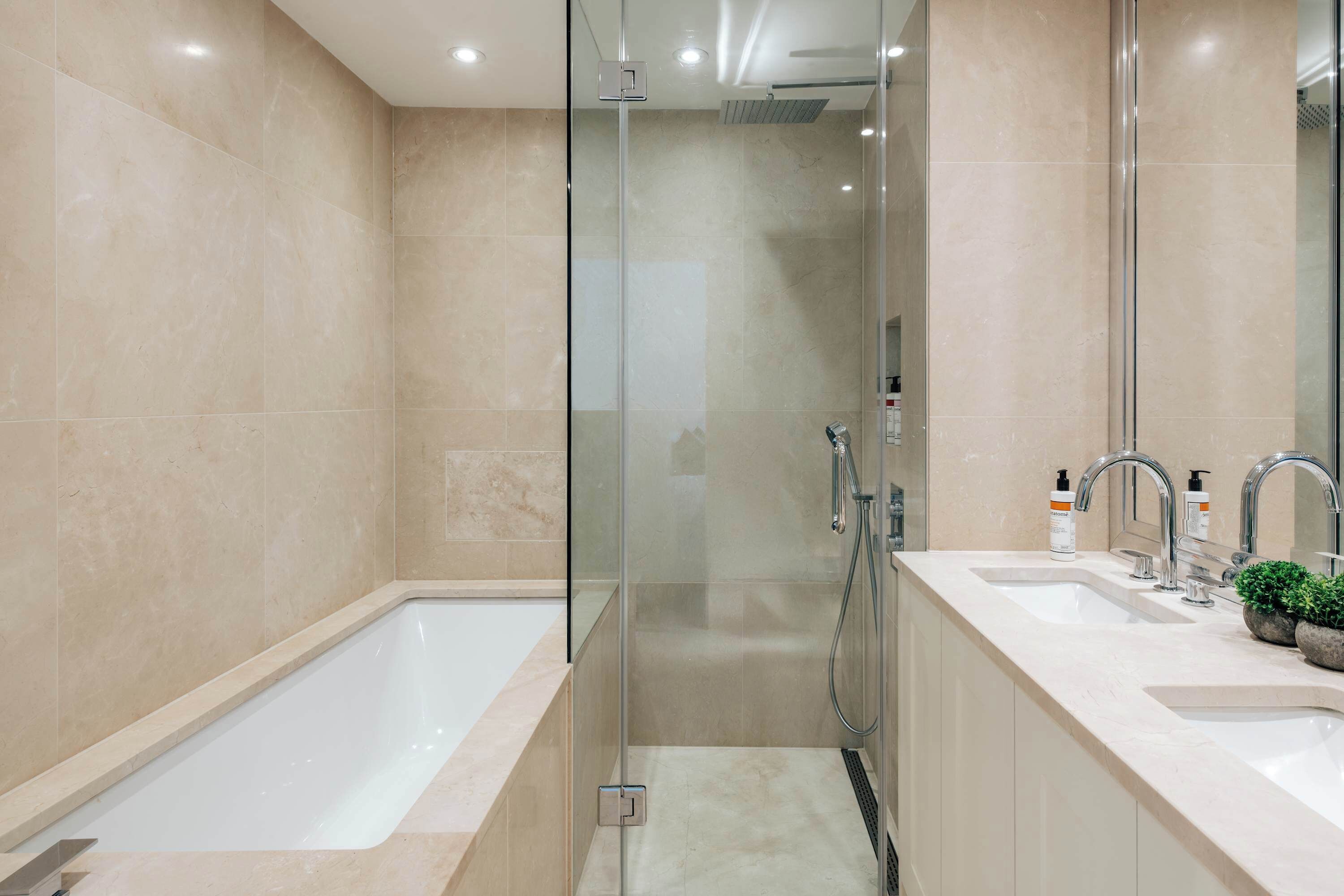 A modern bathroom with a glass-enclosed shower, two sinks, and a large bathtub.
