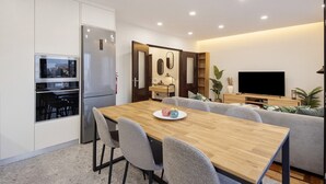 A modern kitchen with built-in appliances, a dining area with a wooden table and chairs, and a living room with a sofa and a flat-screen TV. - Apartment 'Station 54' with Balcony and Wi-Fi (Porto)
