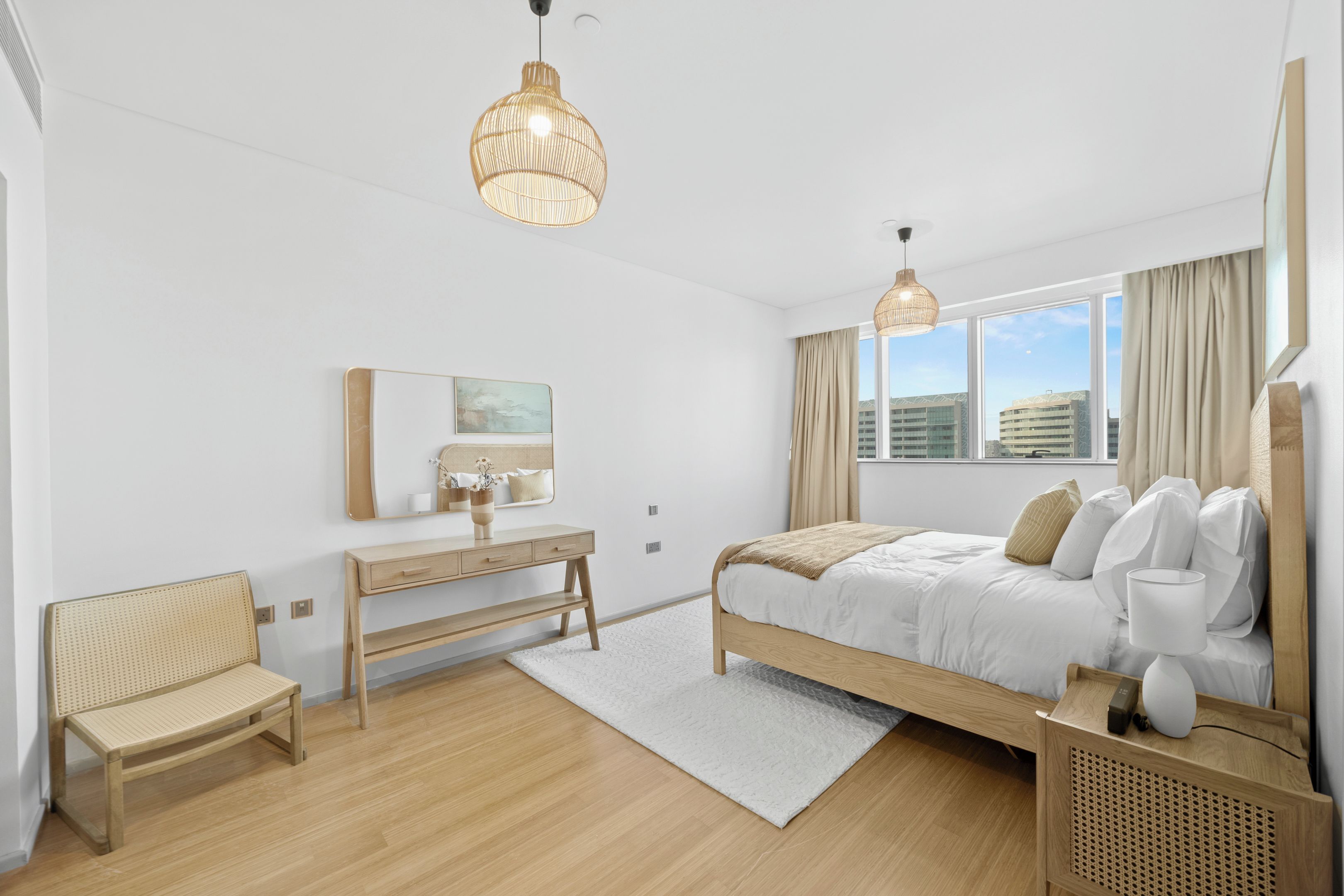 A modern hotel room with a bed, bedside table, chair, and large windows.