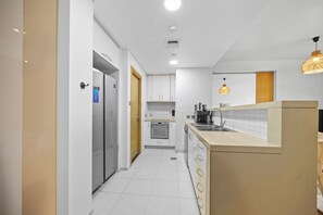 A modern kitchen with white cabinetry, a built-in oven, a stainless steel sink, and a wooden door. - 1011 Bloomfields1BR Al Nada Raha Beach (Madinat Zayed)